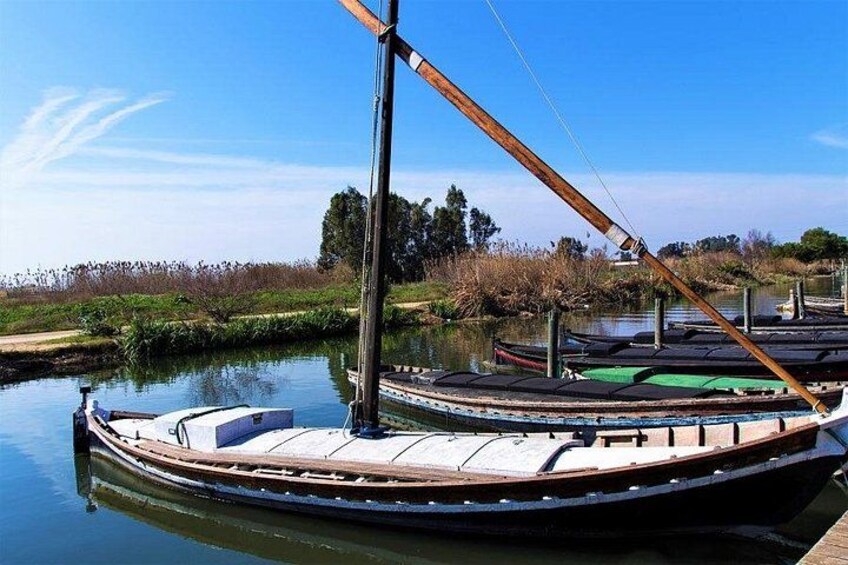 Een roeiboot afgemeerd aan een rustig vaarwater, met een heldere lucht en begroeiing op de achtergrond. 2
