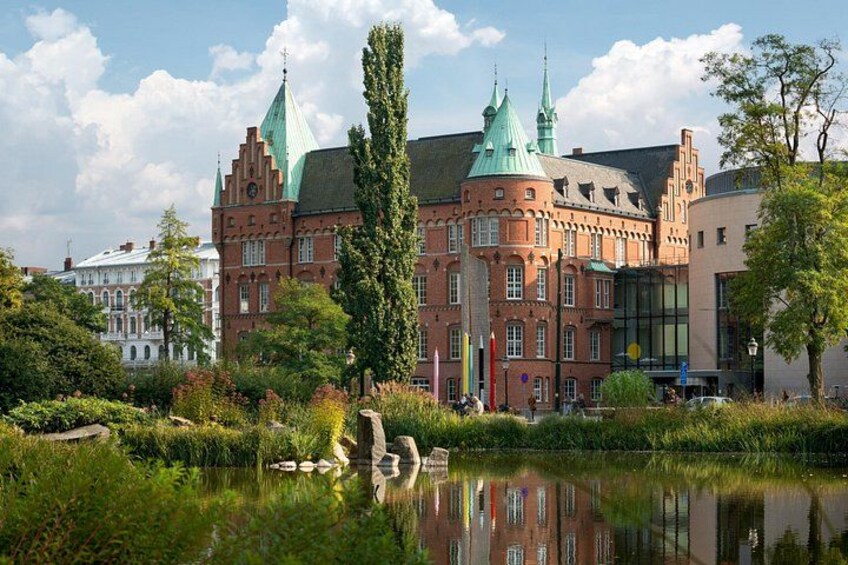 En historisk bygning med grønne tage og en sø i forgrunden. 1