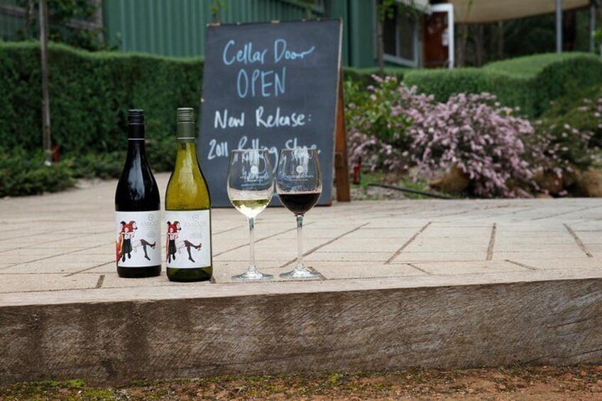 Three wine bottles and two wine glasses on a stone ledge with a sign reading "Cellar Door OPEN New Release 2011 Rolling Stone." 3