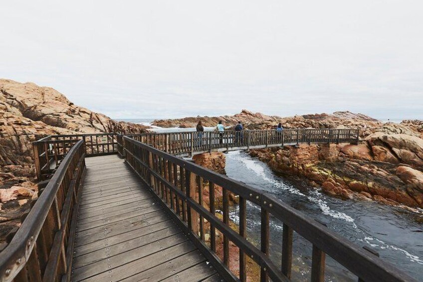 A wooden boardwalk with railings, leading to a rocky coastline with waves crashing against the rocks. 2