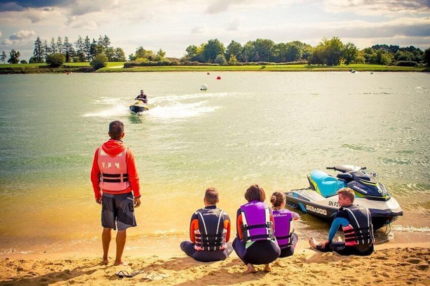 A lake with a jet ski, people on the shore, and a watercraft in the background. 5