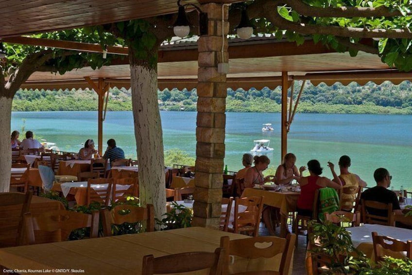 Un restaurante al aire libre con mesas y sillas, con vistas a un lago donde se ve un barco a lo lejos. 2