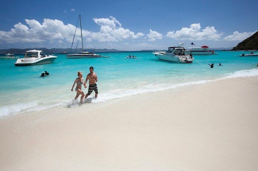 A beach with people walking, boats in the water, and a clear sky. 2