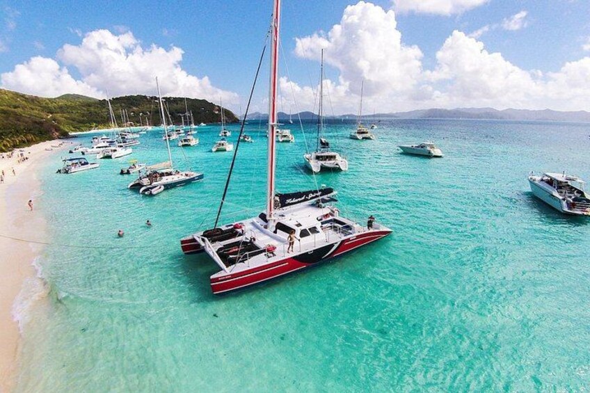 A beach with numerous sailboats anchored in clear turquoise waters. 3