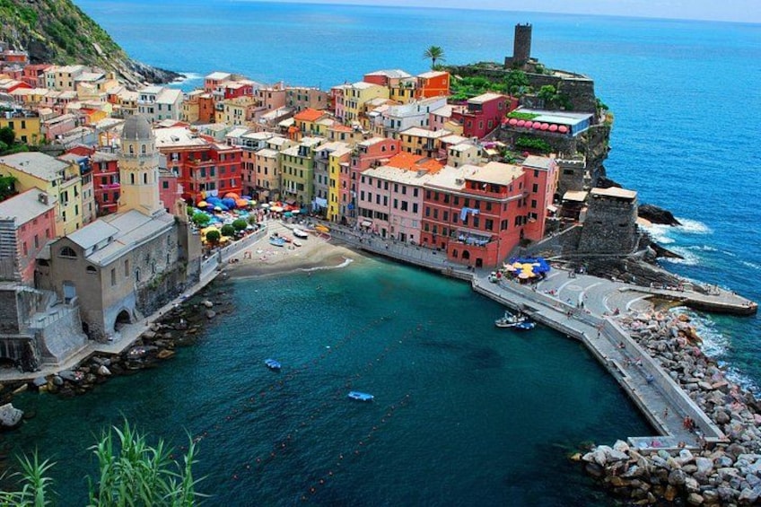 A coastal town with colorful buildings, a beach, and a historic tower. 1
