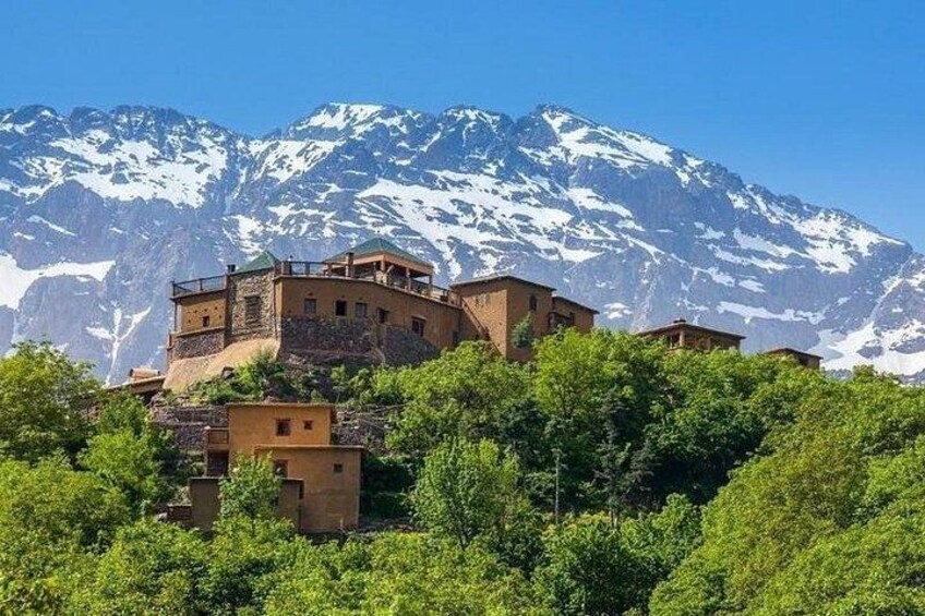 A mountainous village with buildings perched on a hillside, snow-capped peaks in the background. 1