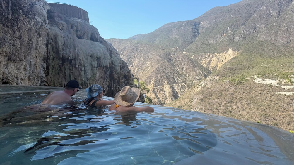 Dos personas en un manantial termal con montañas al fondo. 2