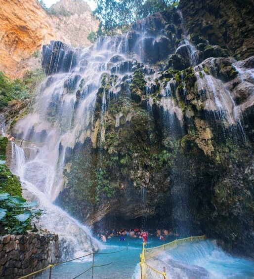 Una cascada escalonada con una poza en la base, rodeada de acantilados rocosos y follaje. 5