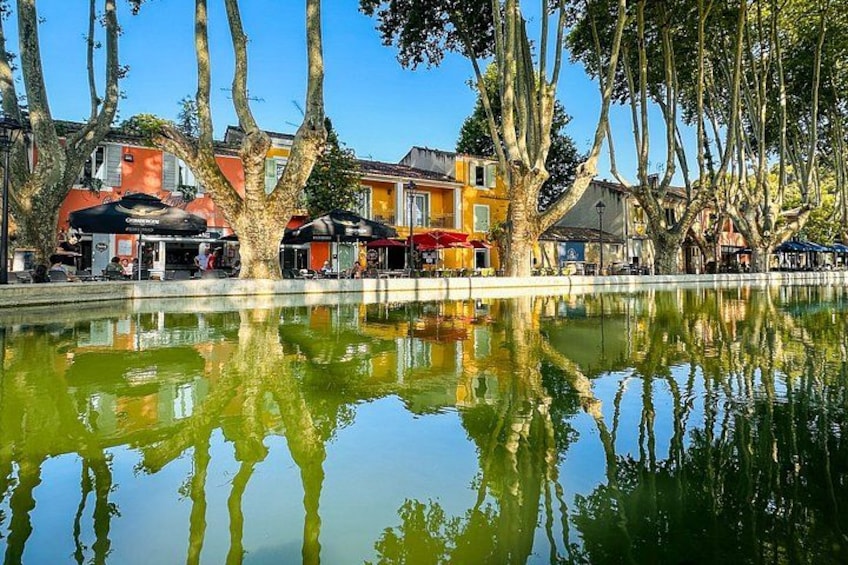 A calm water body reflecting trees and buildings, with outdoor seating under umbrellas. 3