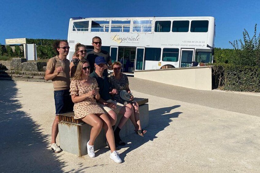 A group of people sitting on a bench in front of a double-decker bus with the name 'Limperial' on it. 3