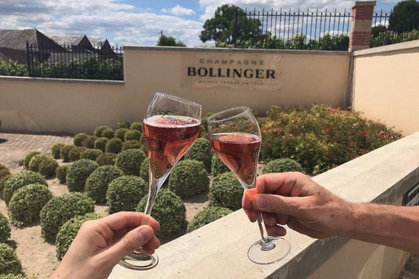 Two people holding wine glasses with a Bollinger champagne sign in the background. 1