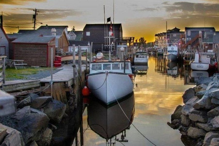 Ein Hafen mit vertäuten Booten, Holzbauten und einem Sonnenuntergang. 1