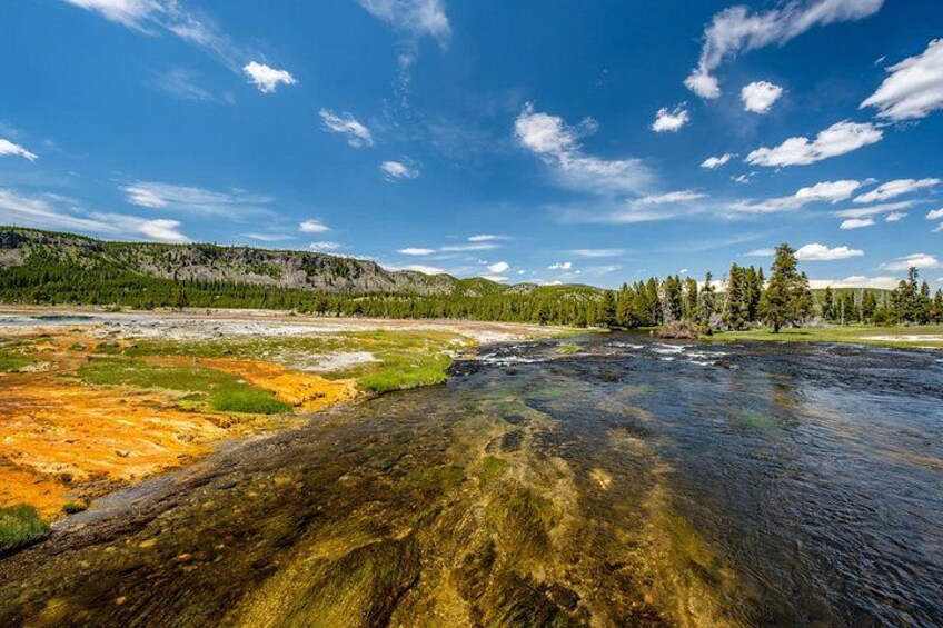 A river with clear water, surrounded by green hills and trees under a blue sky. 3