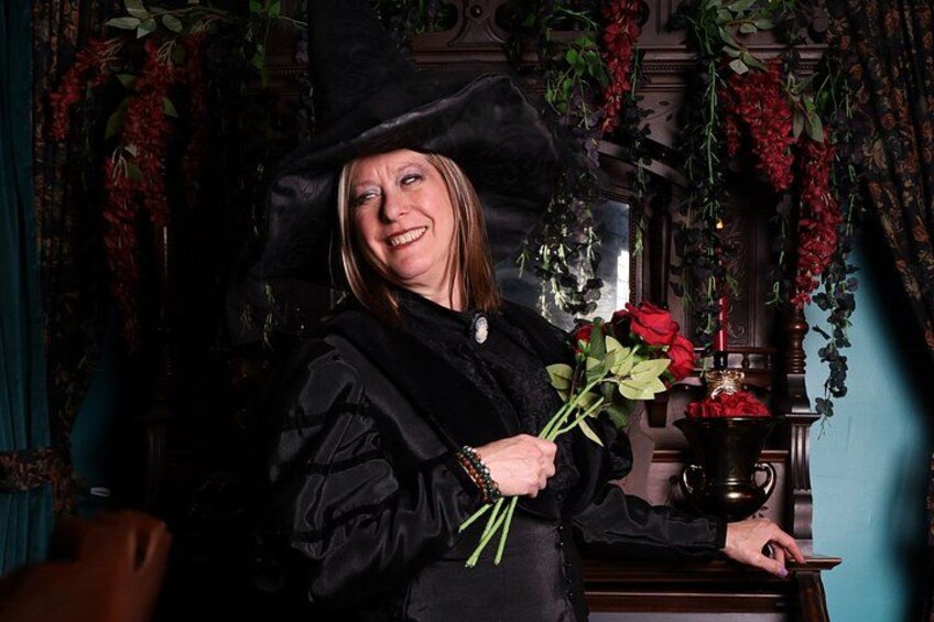 A person in a black robe holding a bouquet of red roses, standing in a room with ornate decorations and a vintage style. 2