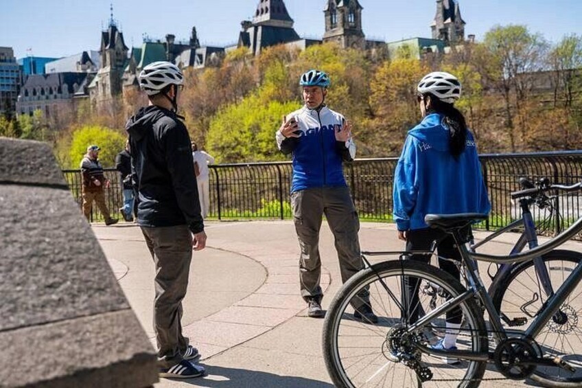 Trois personnes sur un pont, dont une avec un vélo, et un bâtiment historique en arrière-plan. 2