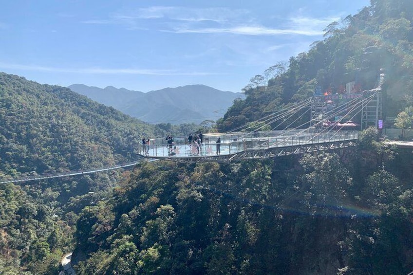 Un puente colgante con barandillas de vidrio, rodeado de montañas verdes y exuberantes. 1