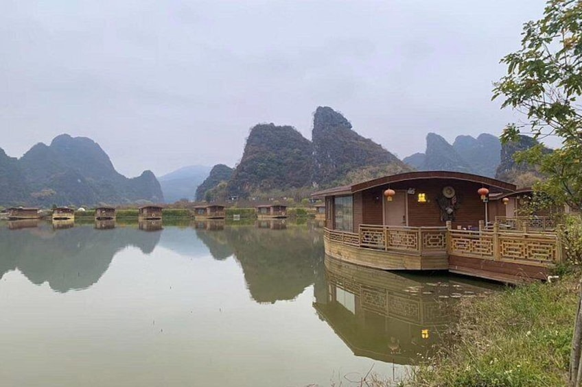 Un cobertizo de madera junto a un río tranquilo, con reflejos de montañas circundantes. 3