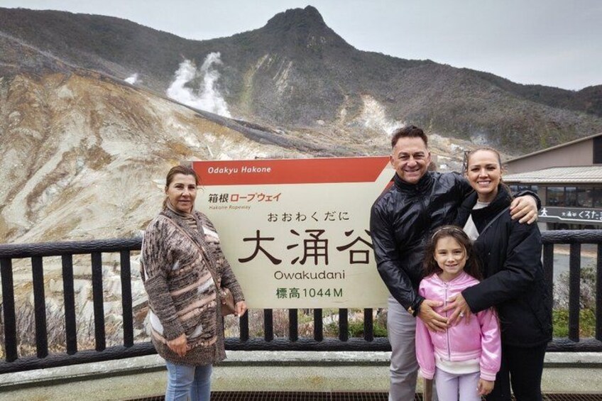 A family posing in front of a signboard with text in Japanese, indicating a location at Owakudani. 2