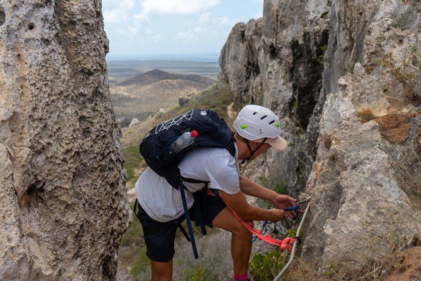 Una persona arrampica una parete rocciosa con uno zaino e attrezzatura da scalata. 1