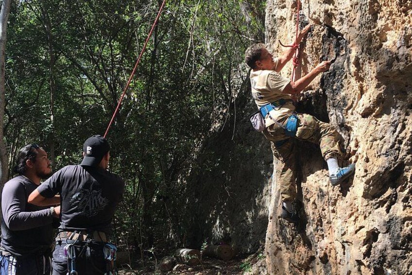 Una persona che fa arrampicata sportiva su una parete rocciosa, con una guida e un assicuratore. 2
