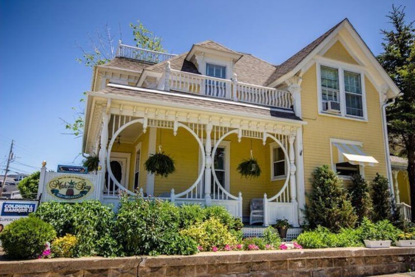 A yellow house with a porch, white railings, and hanging planters. 3