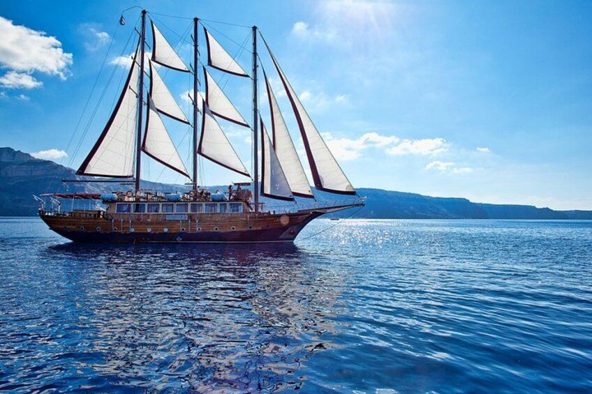 Un barco de vela de madera con varias velas sobre aguas azules tranquilas, con montañas al fondo. 3