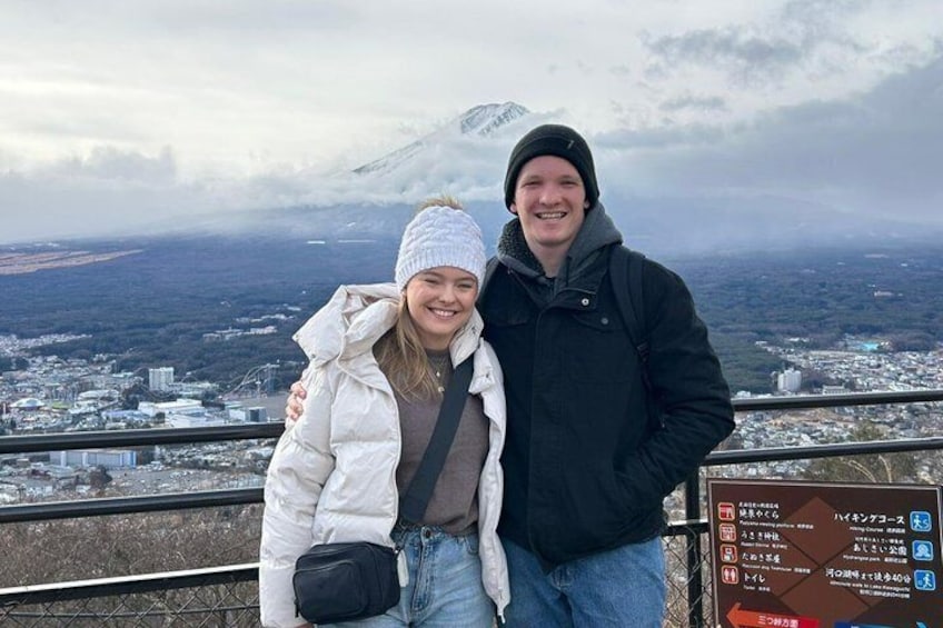Two people standing on a viewing platform with a cityscape and a mountain in the background. 1