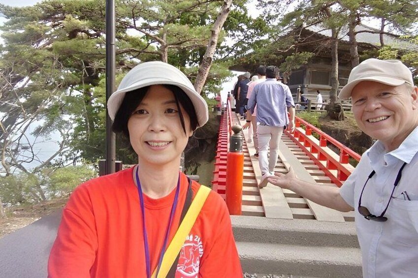 Una persona con camisa roja y gorra blanca de pie sobre un puente de madera con barandillas rojas, contemplando un cuerpo de agua y árboles. 2