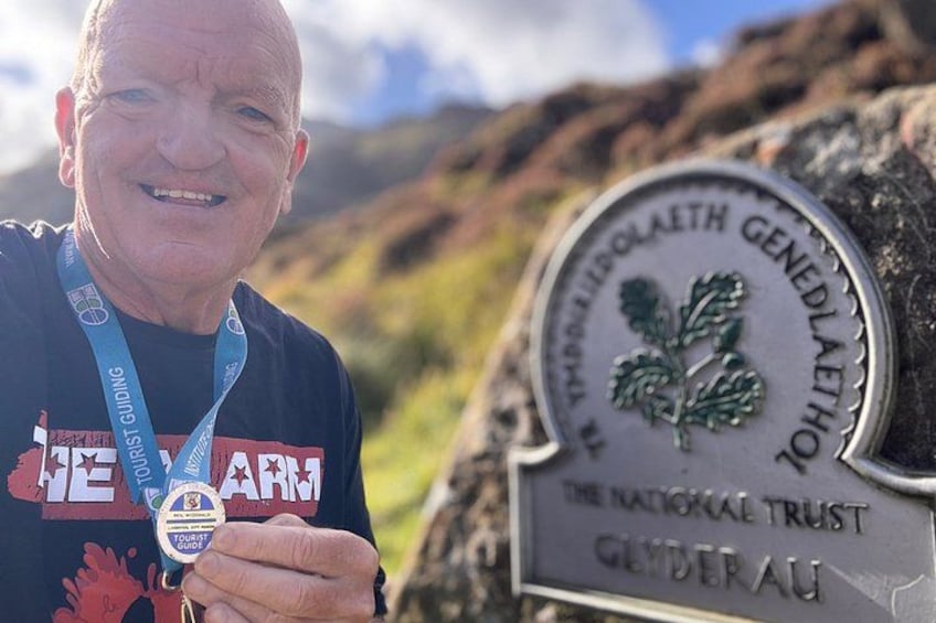 A person holding a medal and a sign with a logo and text. 2