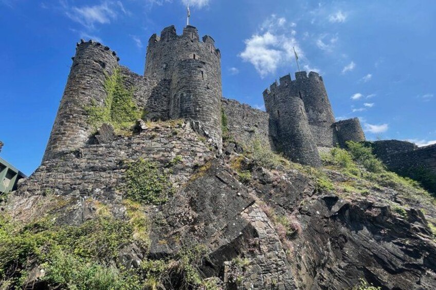 A medieval castle with two prominent towers, surrounded by rocky terrain and greenery. 5