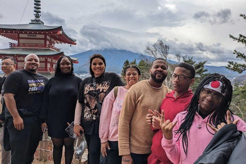 A group of people standing in front of a traditional Japanese pagoda with a mountain in the background. 1
