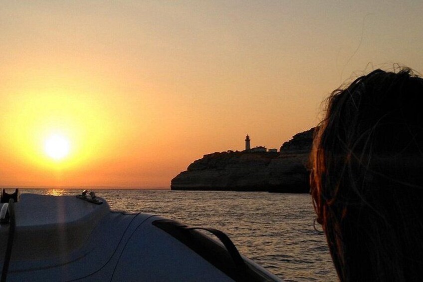 A sunset over water with a rocky outcrop and a lighthouse in the distance. 2