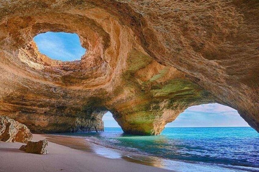 A natural rock formation with a cave-like opening, a sandy beach, and the ocean. 3