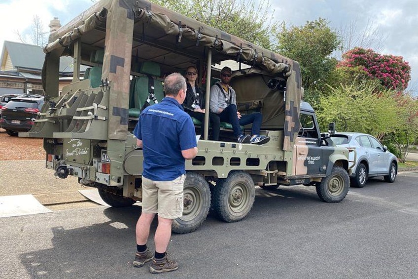 A military-style vehicle with a camouflage pattern, a person standing in front, and another person inside. 3