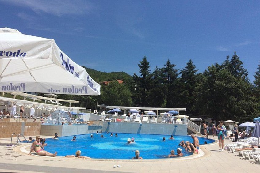A swimming pool with people sunbathing and swimming, surrounded by umbrellas and lounge chairs. 1