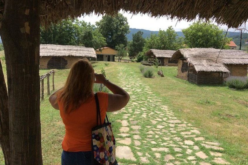 A person taking a photo of traditional thatched-roof huts in a rural setting. 1