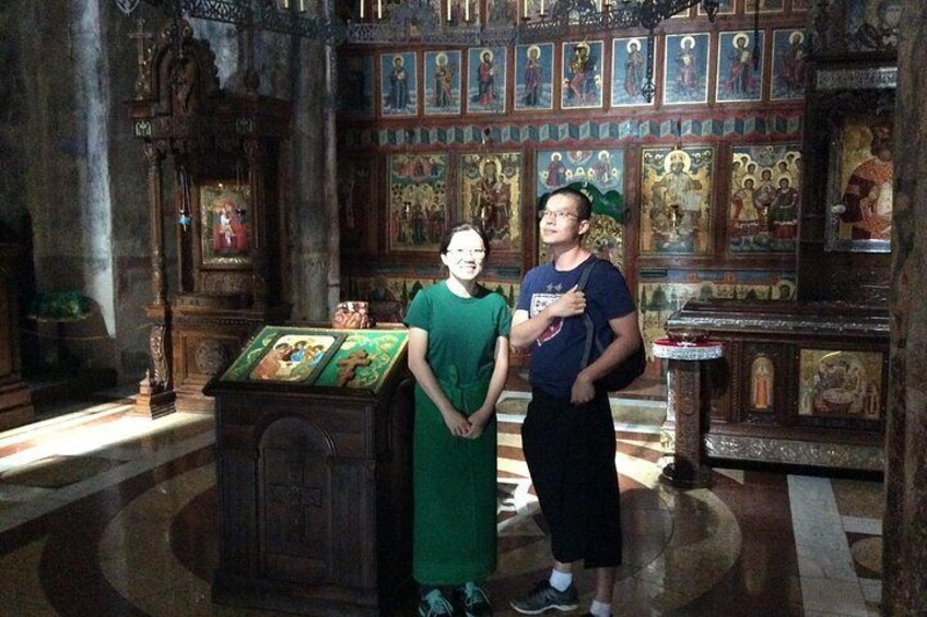 Ein Kircheninneres mit religiösen Ikonen, einem hölzernen Altar und zwei stehenden Personen. 5