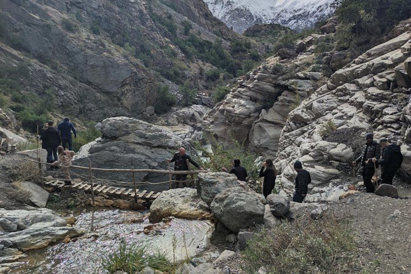 Eine Gruppe von Menschen überquert einen steinigen Bach über eine Brücke. 4