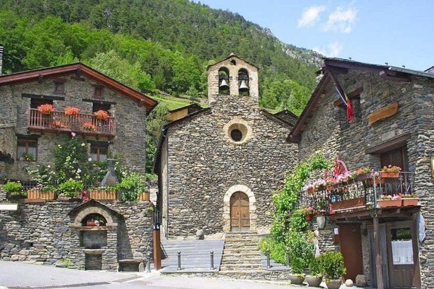 A stone church with a bell tower, surrounded by buildings with balconies and flower boxes. 2