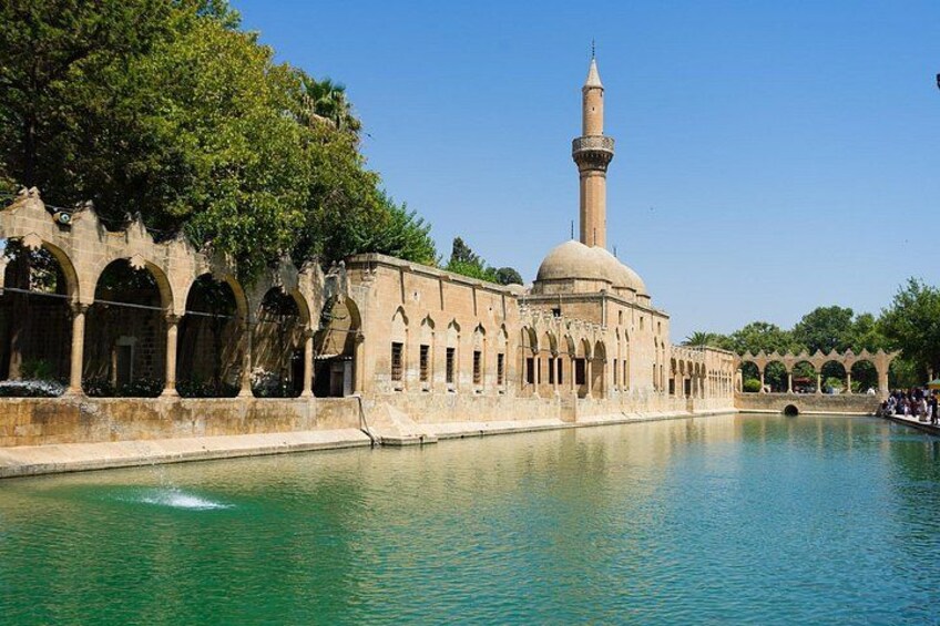 A historic building with arches and a tower, a calm water body, and trees in the background. 3