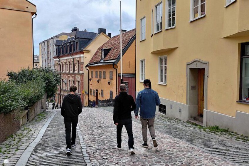 En kullerstensgata med byggnader, en person som går och en parkerad bil. 3