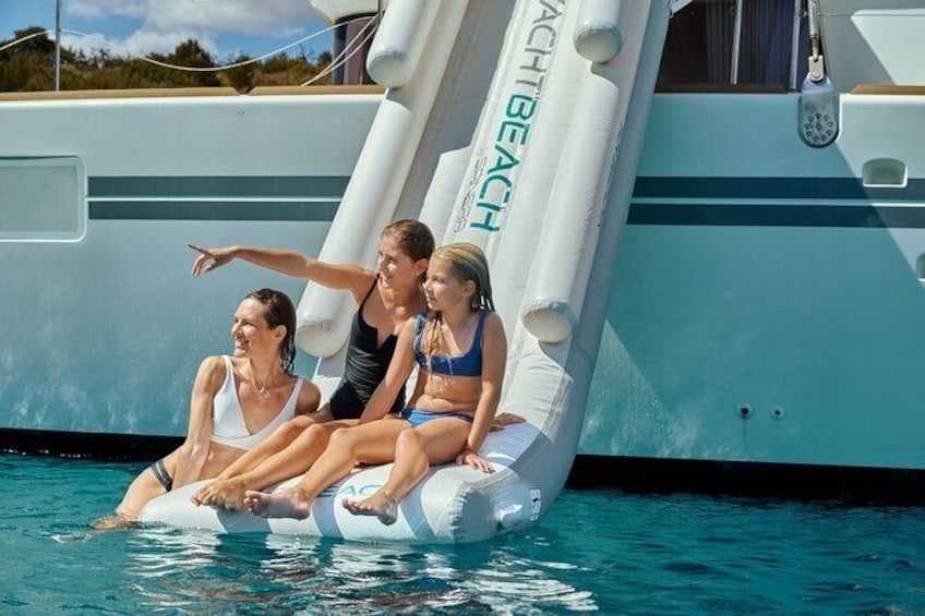 Trois personnes sur une plateforme flottante dans une piscine, avec un yacht en arrière-plan. 1