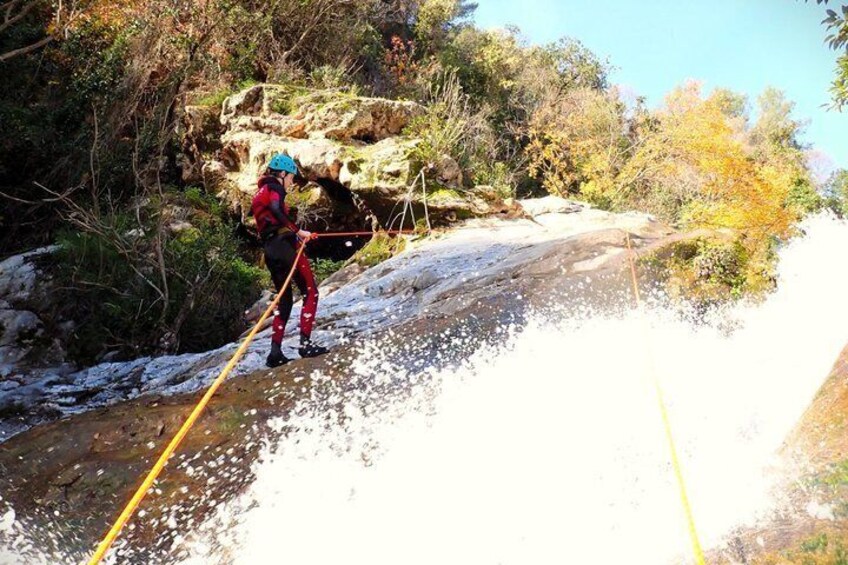 A person in red and black gear crossing a shallow stream with a yellow rope. 5