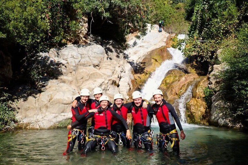 A group of people in red life jackets and helmets standing in a river with a waterfall in the background. 3