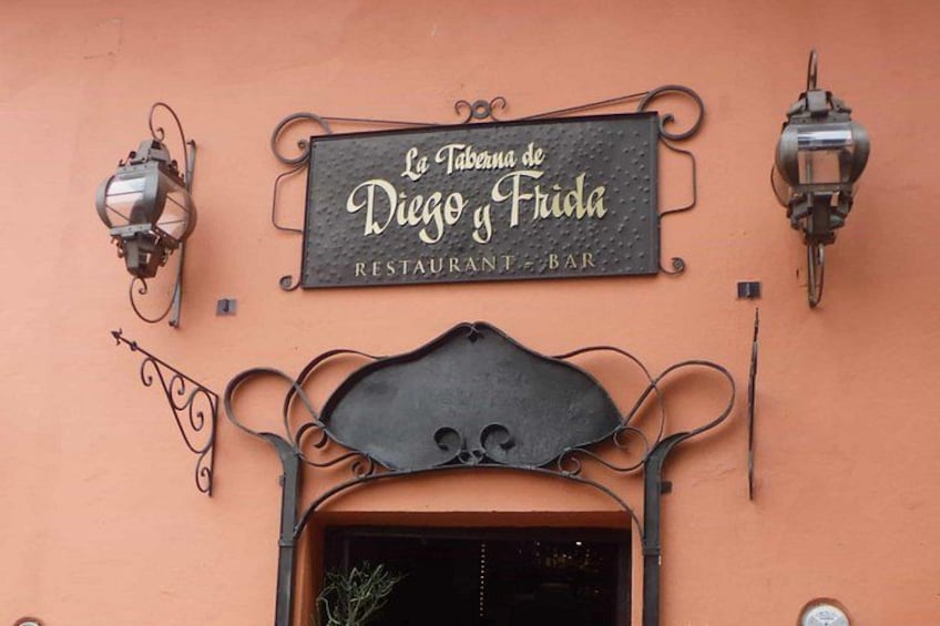 A restaurant sign with a decorative metal frame and two wall-mounted lanterns. 1