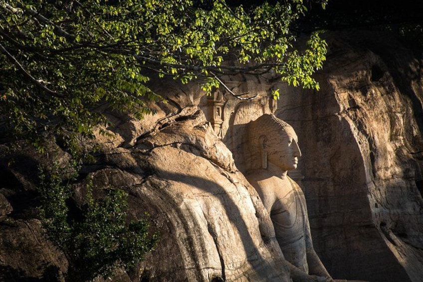 A large rock-cut statue of a seated figure, surrounded by natural rock formations and foliage. 4