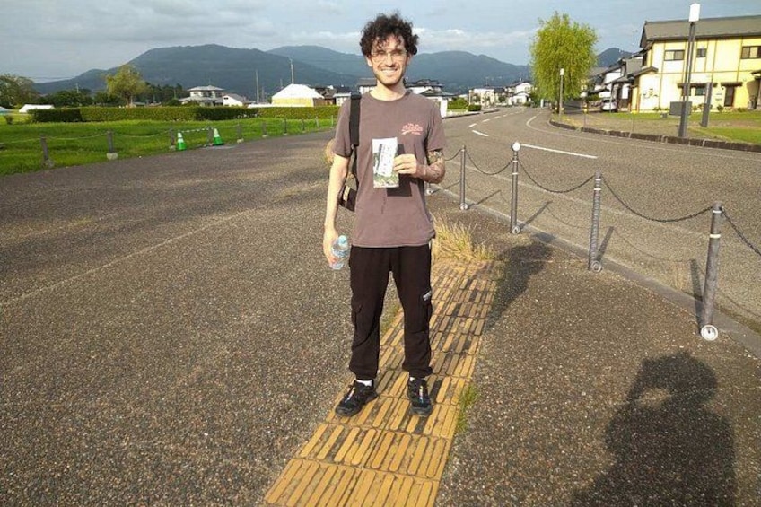 A person standing on a road with a yellow tactile paving strip, holding a booklet and a water bottle. 4