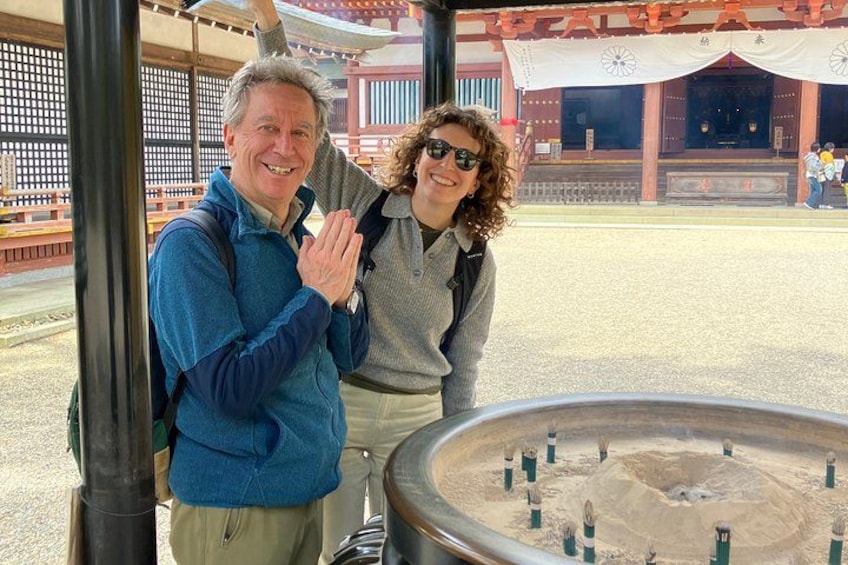 Two people standing in front of a traditional Japanese building with a large, circular stone structure in the foreground. 1