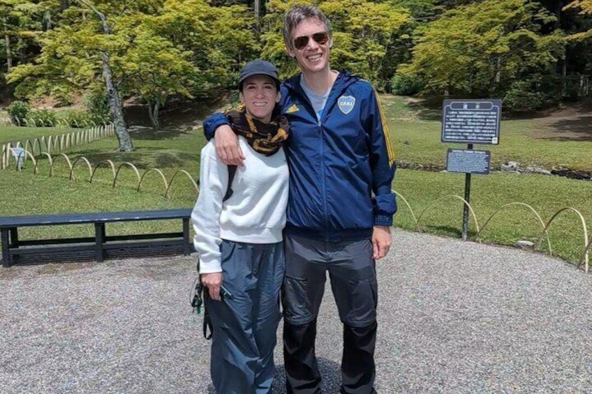 Two people standing in a park with a signboard and a fenced area in the background. 4