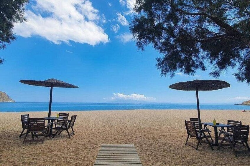 Une plage avec deux tables et des chaises sous des parasols, une promenade en bois et un ciel bleu dégagé. 3